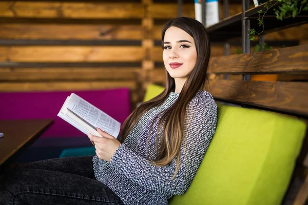 Lächelnde junge Frau liest Buch im Café oder am Arbeitsplatz — Stockfoto