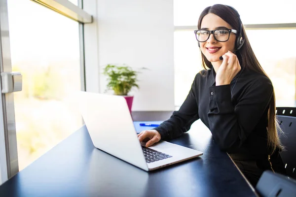 Operadora de atención al cliente femenina con auriculares y sonriente en la oficina — Foto de Stock