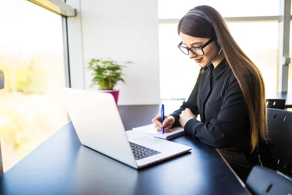 Opgewonden jonge vrouw manager voor het maken van notities op goed nieuws op de headset en laptop in kantoor — Stockfoto