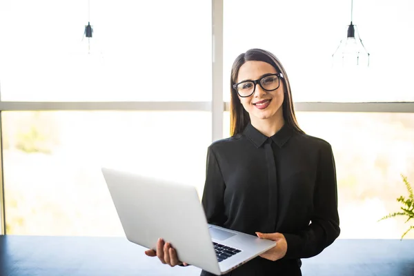 Portret udanego interesu trzyma laptopa w jej ręce. Szczęśliwy piękna kobieta pewnie stoi w biurze z notebooka. — Zdjęcie stockowe
