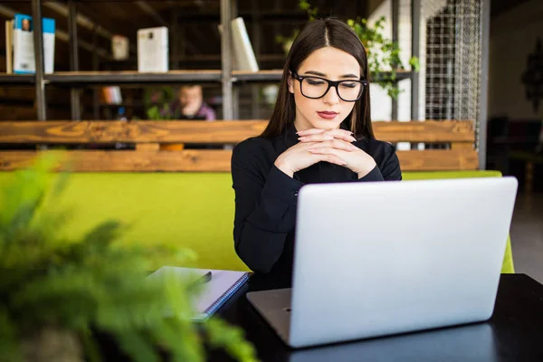 Glad ung vacker affärskvinna i glasögon tittar på kamera med leende medan du sitter på hennes arbetsplats — Stockfoto