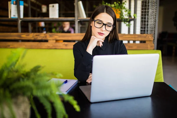 Glad ung vacker affärskvinna i glasögon tittar på kamera med leende medan du sitter på hennes arbetsplats — Stockfoto
