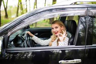 Çekici kız modern bir arabada oturuyor. O pencereden bakarak ve iyi işaret gösteren.