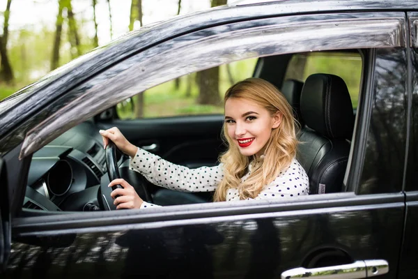 Vista trasera de la atractiva joven en ropa casual mirando por encima de su hombro mientras conduce un coche — Foto de Stock