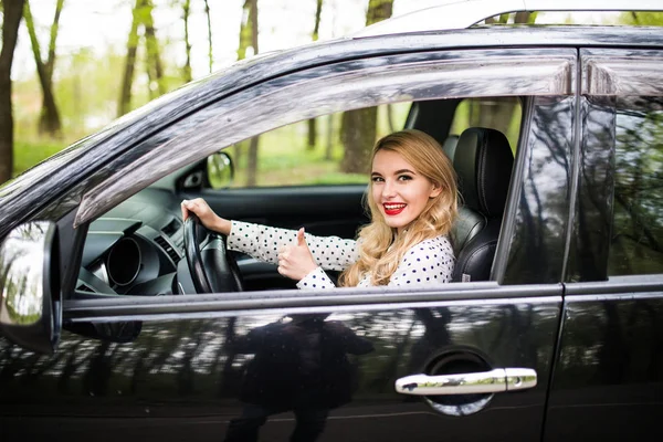 Mujer sentada en el coche y mostrando pulgares hacia arriba en la carretera — Foto de Stock