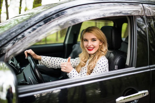 Mujer sentada en el coche y mostrando pulgares hacia arriba en la carretera — Foto de Stock