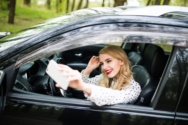 Χαμογελώντας νεαρή γυναίκα λήψη selfie φωτογραφία με έξυπνο τηλέφωνο φωτογραφική μηχανή στο αυτοκίνητο — Φωτογραφία Αρχείου