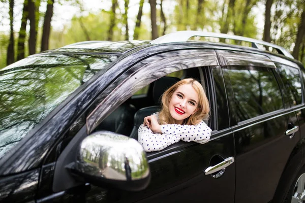 Mujer joven sentada en el coche nuevo y mirar por la ventana — Foto de Stock