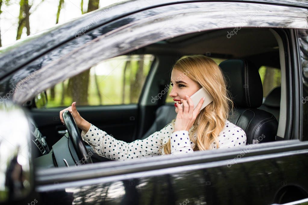 Beautiful woman is talking on the mobile phone and smiling while sitting in the car