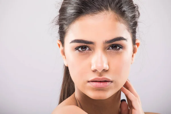 Pretty girl with big eyes and dark eyebrows, with naked shoulders, looking at camera and smiling gray studio background Royalty Free Stock Photos