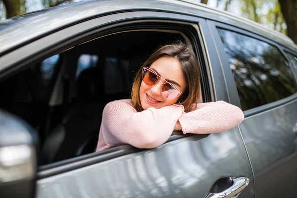 Attrayant jeune femme regarde par la fenêtre de la voiture en attendant un voyage et sourire — Photo