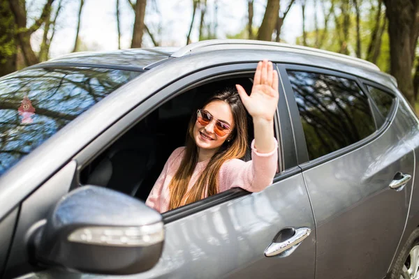 Belles jeunes femmes gaies regardant la caméra avec le sourire et agitant tout en étant assis dans sa voiture — Photo