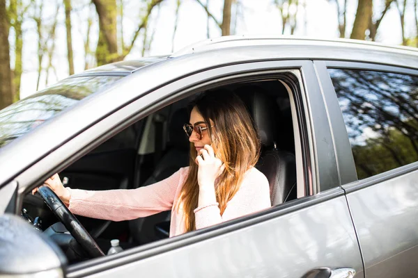 Wanita muda mengendarai mobil dan berbicara pada ponsel berkonsentrasi pada jalan — Stok Foto
