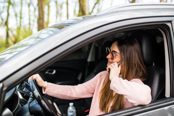 Linda feliz e rindo com todos os dentes jovem mulher caucasiana é dirigir no carro e falando no telefone móvel . — Fotografia de Stock