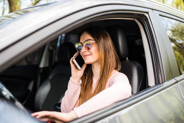 Jeune femme avec la main sur le volant en utilisant le téléphone portable tout en conduisant sa voiture — Photo