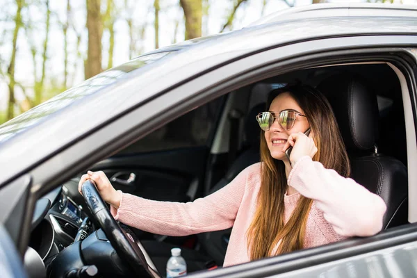 Женщина разговаривает по телефону во время вождения своей машины на улице — стоковое фото