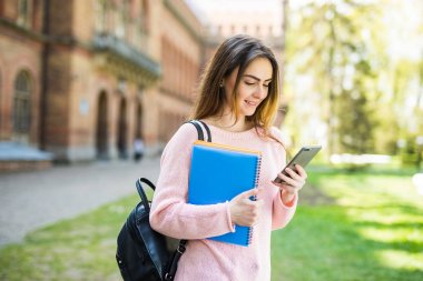 Kahve ve kitap çantası elinde telefon ile kampüste ile gülümseyen Amerikan Üniversitesi Öğrenci