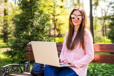 Park Bank güneşli bir günde bir dizüstü bilgisayar ile genç kadın