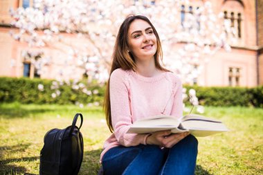 genç, çekici kız öğrenci yeşil çim ve çiçek ağaç çerçevede kitap okur