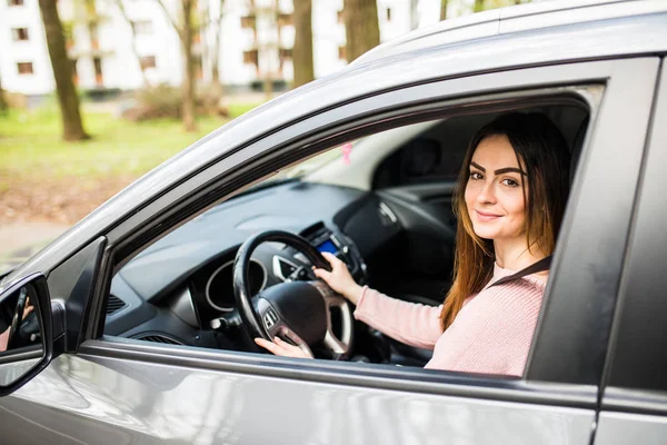 Mujer joven segura y hermosa en ropa casual mirando por encima de su hombro mientras conduce un coche —  Fotos de Stock