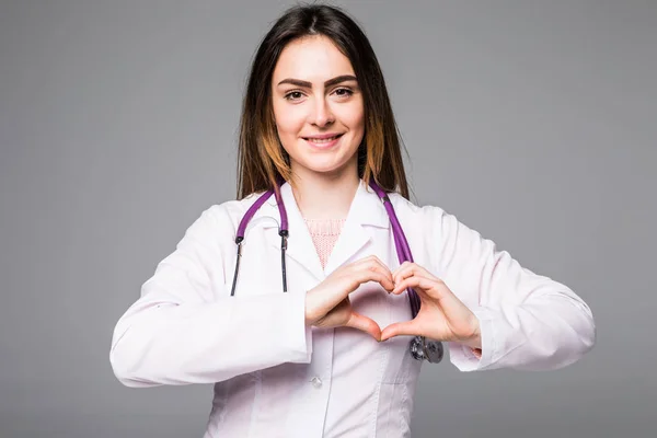 Médico poniendo sus manos en forma de corazón aislado sobre fondo gris — Foto de Stock