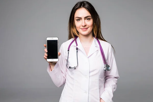 Młoda kobieta lekarz stałego i trzymając pusty ekran telefon komórkowy na białym tle — Zdjęcie stockowe