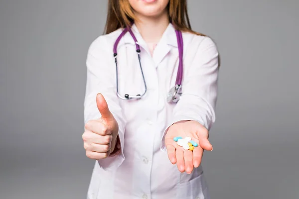 Kvinna sjuksköterska visar piller i hand isolerad på grå — Stockfoto