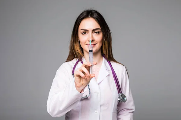 Portret młoda lekarka uśmiecha się ze strzykawką w ręku. Portret lekarza piękną kobietę na szary — Zdjęcie stockowe