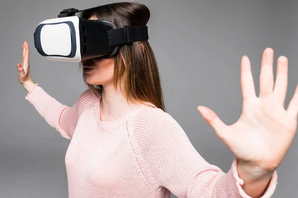 Atractiva mujer joven mirando a través de auriculares de realidad virtual, tiro interior sobre fondo blanco. modelo femenino de aspecto caucásico con gafas VR . — Foto de Stock