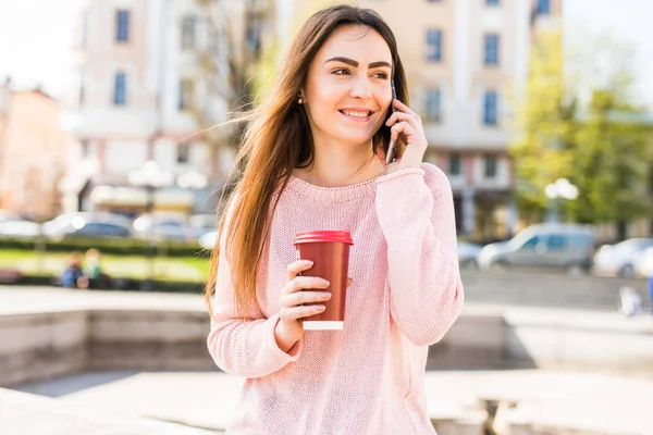 Retrato de chica feliz hablando por teléfono y tomando café en la soleada calle de la ciudad — Foto de Stock