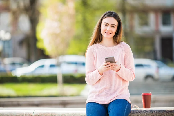 Молодая женщина с телефоном просматривать в Интернете и пить кофе на улице города — стоковое фото