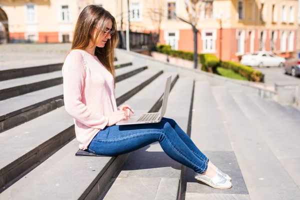 Retrato de uma jovem mulher feliz sentada nas escadas da cidade e usando computador portátil — Fotografia de Stock