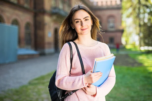 Студентка университета выглядит счастливой, улыбаясь с книгой или блокнотом в кампусе парка . — стоковое фото
