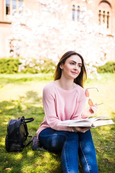 Молодая красивая студентка в летнем парке читает книгу на траве — стоковое фото