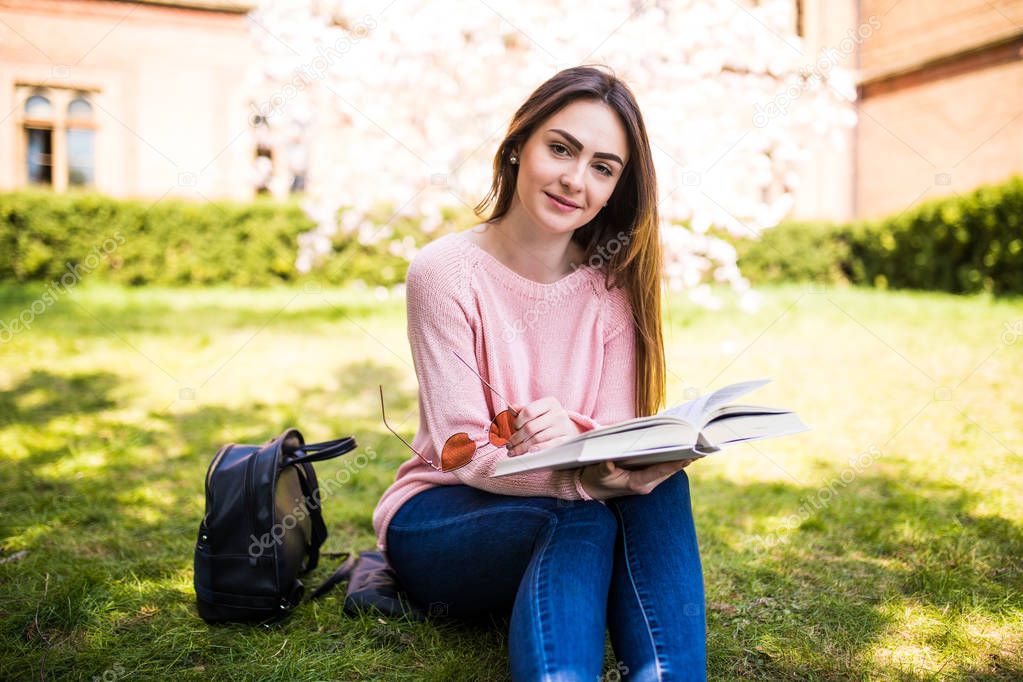 young woman reading book in park on the grass sunny day