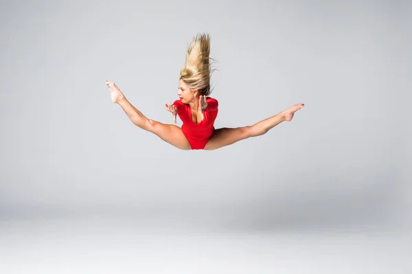 年轻漂亮金发苗条女人，跳跃和做体操在白色背景上的红色身体 — 图库照片