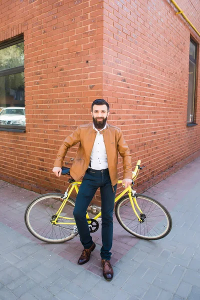 Jovem homem elegante com uma barba sentada em uma bicicleta de fundo de tijolo — Fotografia de Stock