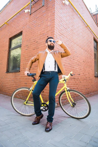 Bisiklet bir tuğla zemin üzerine oturan güneş gözlüğü sakallı genç şık adam — Stok fotoğraf