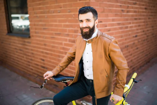 Jovem homem elegante com uma barba sentada na bicicleta em um fundo de tijolo — Fotografia de Stock