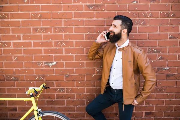 流行に敏感な若い男が壁に固定自転車と電話を話す — ストック写真