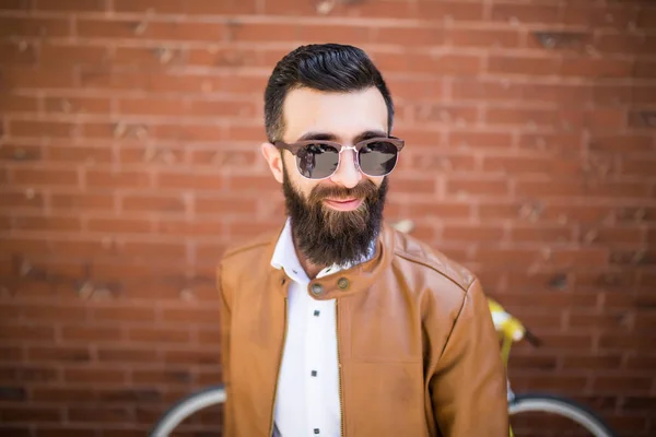 Retrato de cerca de un hombre barbudo brutal sobre fondo de pared de ladrillo. Joven hipster elegante posando en la calle . — Foto de Stock