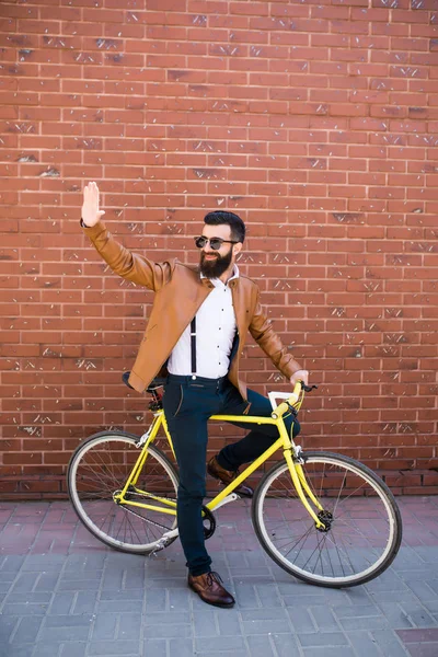 Feliz jovem hipster homem com bicicleta de engrenagem fixa acenando mão na rua da cidade — Fotografia de Stock