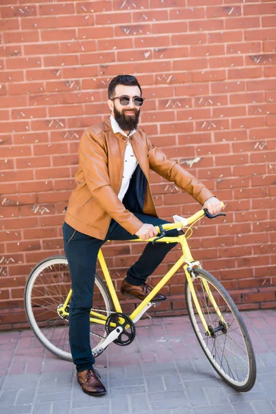Serin genç sakallı hippi yanı sıra tuğla duvar sokak düzenleme bisikletle — Stok fotoğraf