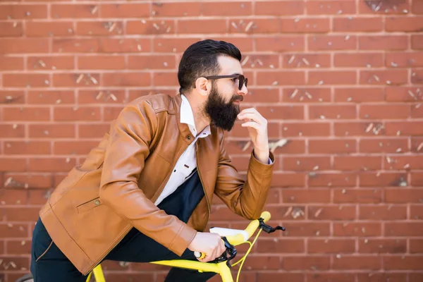 Homem bonito jovem com uma barba contra a parede de tijolo senta-se em uma bicicleta — Fotografia de Stock