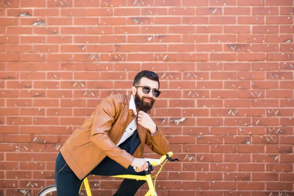 Homem bonito jovem com uma barba contra a parede de tijolo senta-se em uma bicicleta — Fotografia de Stock