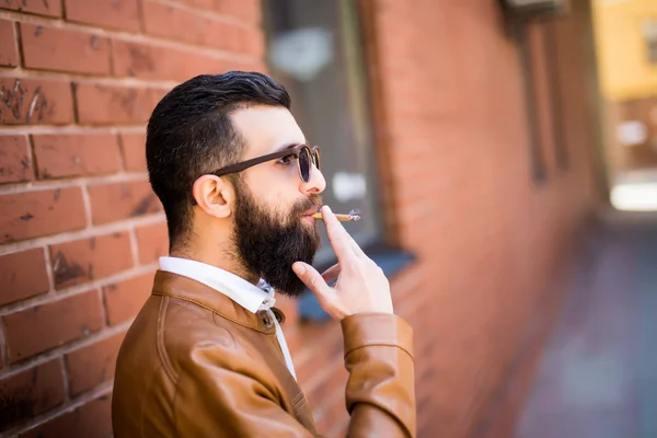 Βάναυση Καυκάσιος hipster κάπνισμα πούρων στον εξωτερικό τοίχο από τούβλα — Φωτογραφία Αρχείου