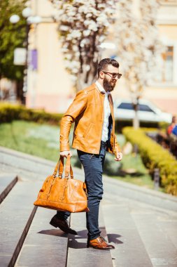 Yakışıklı genç adam şehir açık havada çantası ile merdivenlerde yürürken güneş gözlüğü sakallı