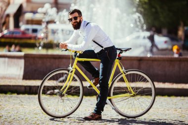 Yakışıklı hipster genç adam Onun Bisiklet açık havada çeşmeler yakın otururken kameraya bakan sakallı
