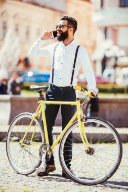 Mobil telefonda konuşurken ve bisikletine sokakta yanında otururken gülümseyen adam genç sakallı