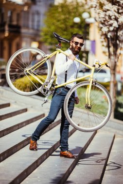 Düzeltme Bisiklet sakallı adam. Onun Bisiklet omuz üzerinde taşıyan ve uzak açık havada şehir merdivenlerde yürürken bakarak kendine güvenen genç sakallı adam görünümünü